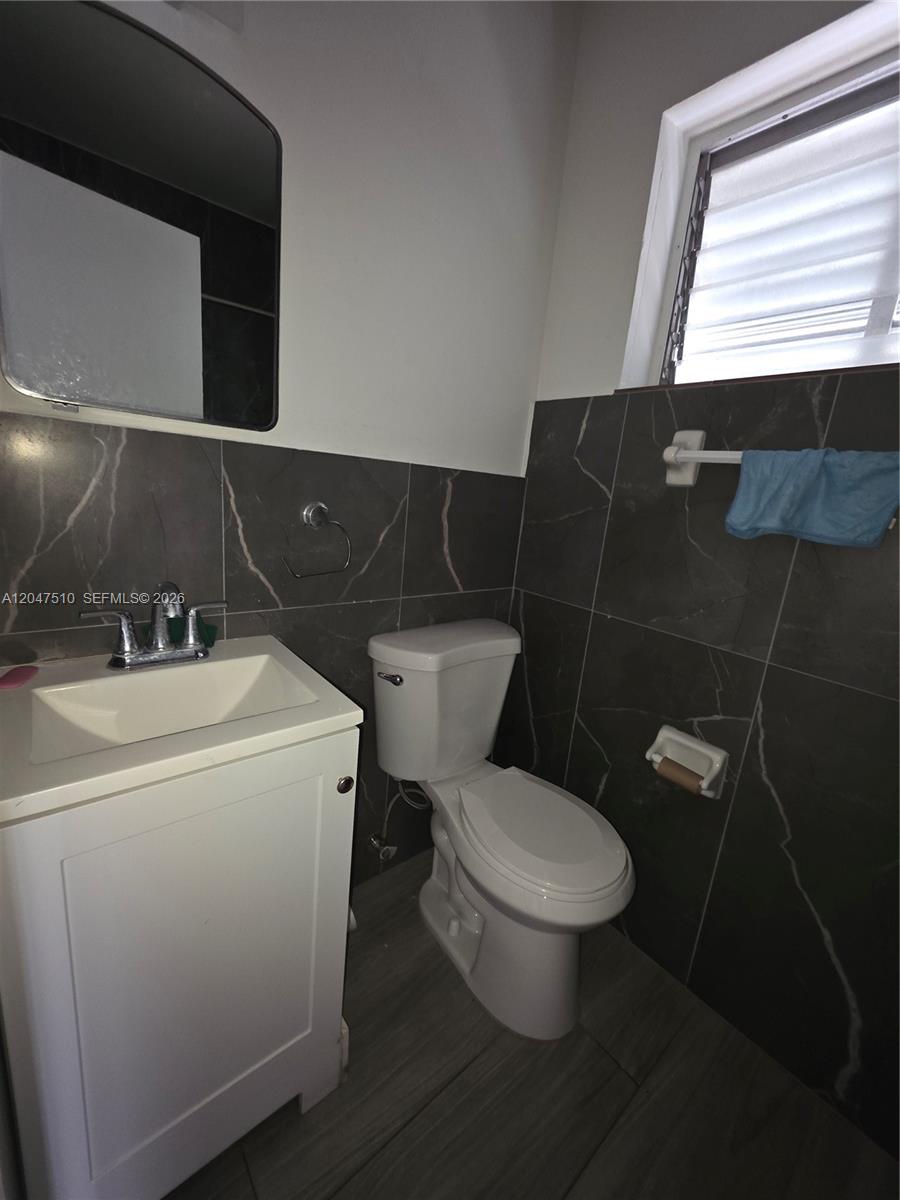A bathroom features a white vanity, a toilet, and dark marble-patterned wall tiles — 15 Esplanade Dr # B, Miami Springs FL 33166, MIAMI SPRINGS, FL