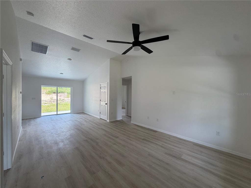 An empty living room features vaulted ceilings, a ceiling fan, and light wood-look flooring — 2691 SW 148TH COURT, OCALA, FL