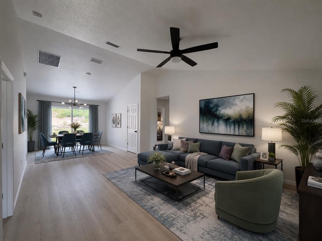 A living room and dining area with light wood floors, a blue sectional, and vaulted ceilings — 2691 SW 148TH COURT, OCALA, FL