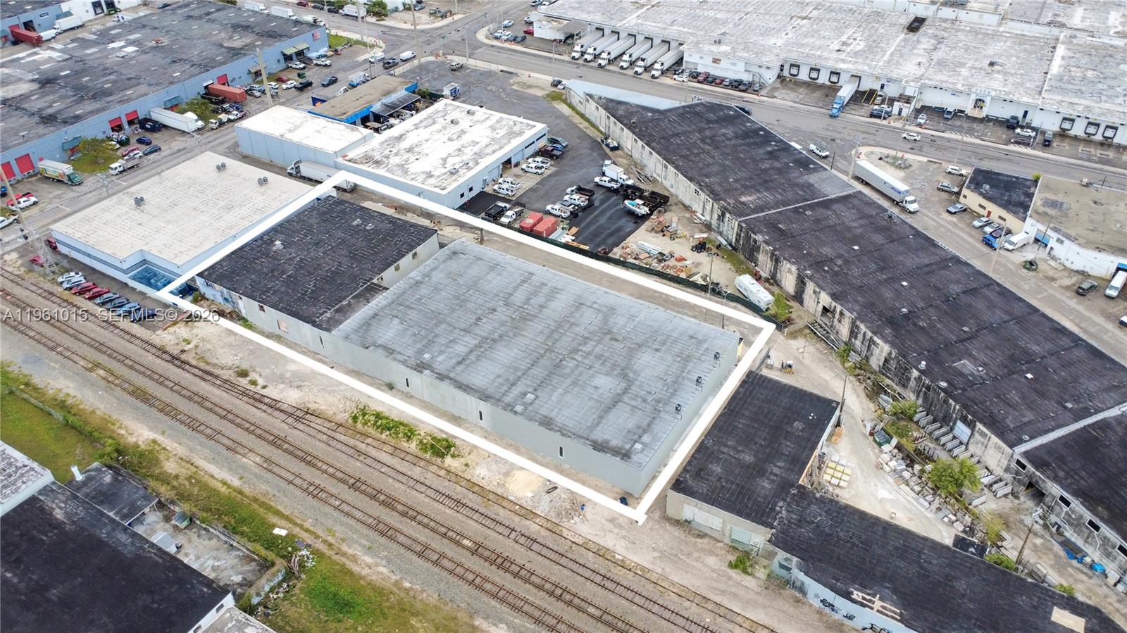 An aerial view shows a rectangular industrial warehouse building situated next to railroad tracks — 7000 NW 37th Ct, Hialeah FL 33147, HIALEAH, FL