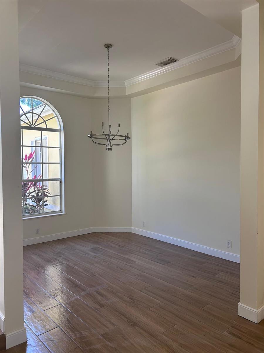 An empty dining room features wood-look tile flooring, a tray ceiling, and a large arched window — 8992 Lakes Boulevard, West Palm Beach FL 33412, WEST PALM BEACH, FL