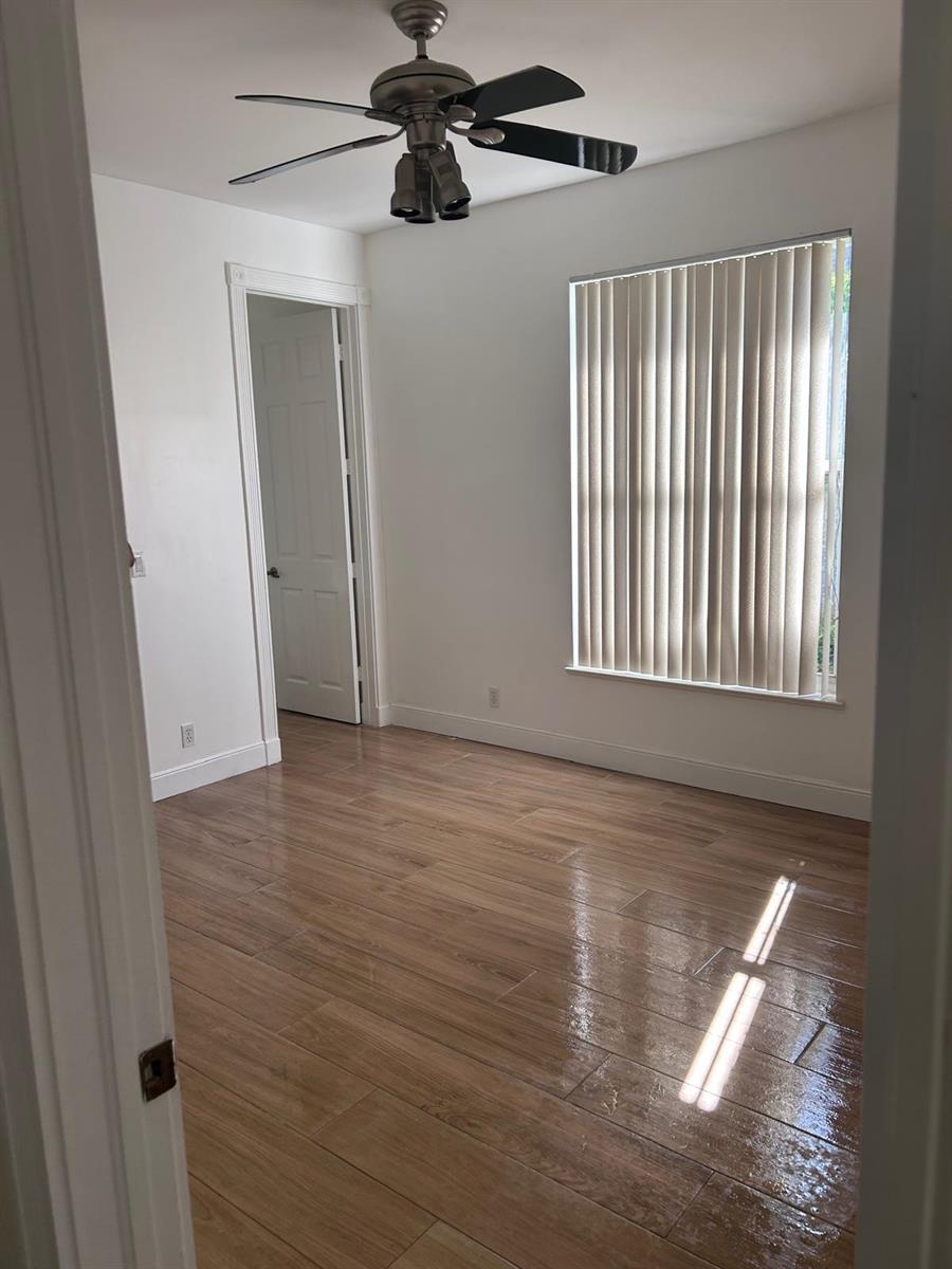 An empty bedroom features wood-look tile flooring, white walls, a ceiling fan, and vertical blinds — 8992 Lakes Boulevard, West Palm Beach FL 33412, WEST PALM BEACH, FL
