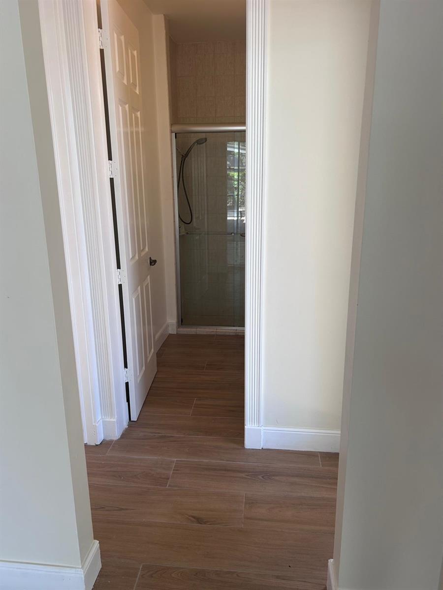 A hallway with wood-look tile flooring leads to a glass-enclosed shower stall — 8992 Lakes Boulevard, West Palm Beach FL 33412, WEST PALM BEACH, FL