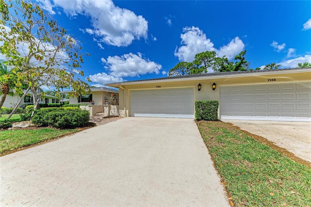 A low-angle exterior view of a single-story duplex with two white garage doors — 7160 FAIRWAY BEND CIR, SARASOTA, FL