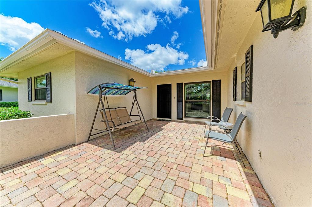 A paved patio features a swing set and two chairs against a stucco house exterior — 7160 FAIRWAY BEND CIR, SARASOTA, FL