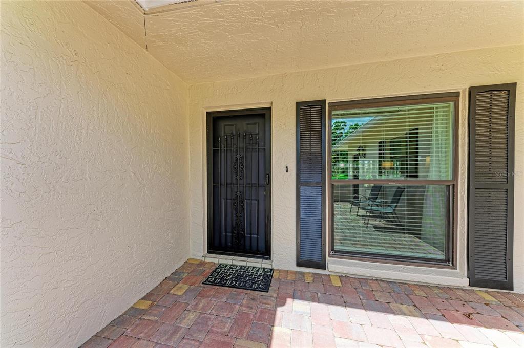 A covered entryway features a brick paver floor, a security screen door, and a window — 7160 FAIRWAY BEND CIR, SARASOTA, FL