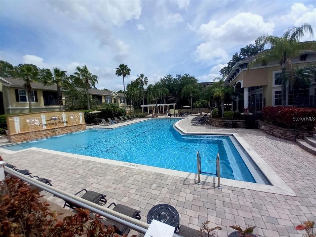 A swimming pool with a fountain feature is surrounded by a paved deck and buildings — 10025 COURTNEY PALMS BOULEVARD UNIT 204, TAMPA, FL
