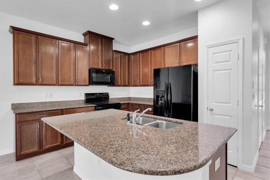 A kitchen features brown wood cabinets, granite countertops, a center island, and black appliances — 4057 71ST TERRACE N, PINELLAS PARK, FL