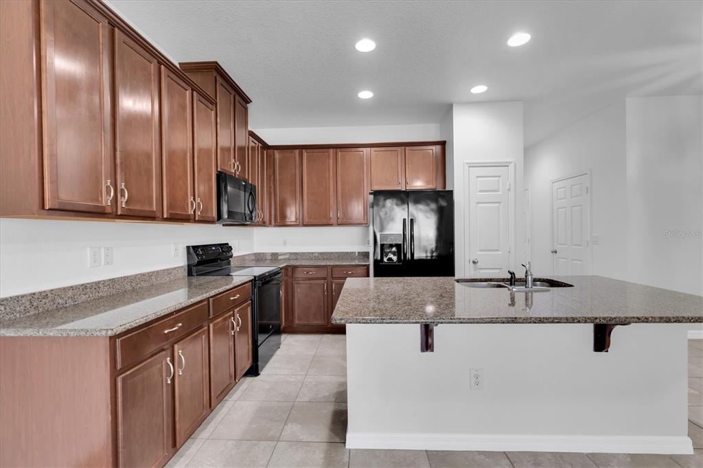 A kitchen features wood cabinets, granite countertops, an island with a sink, and black appliances — 4057 71ST TERRACE N, PINELLAS PARK, FL