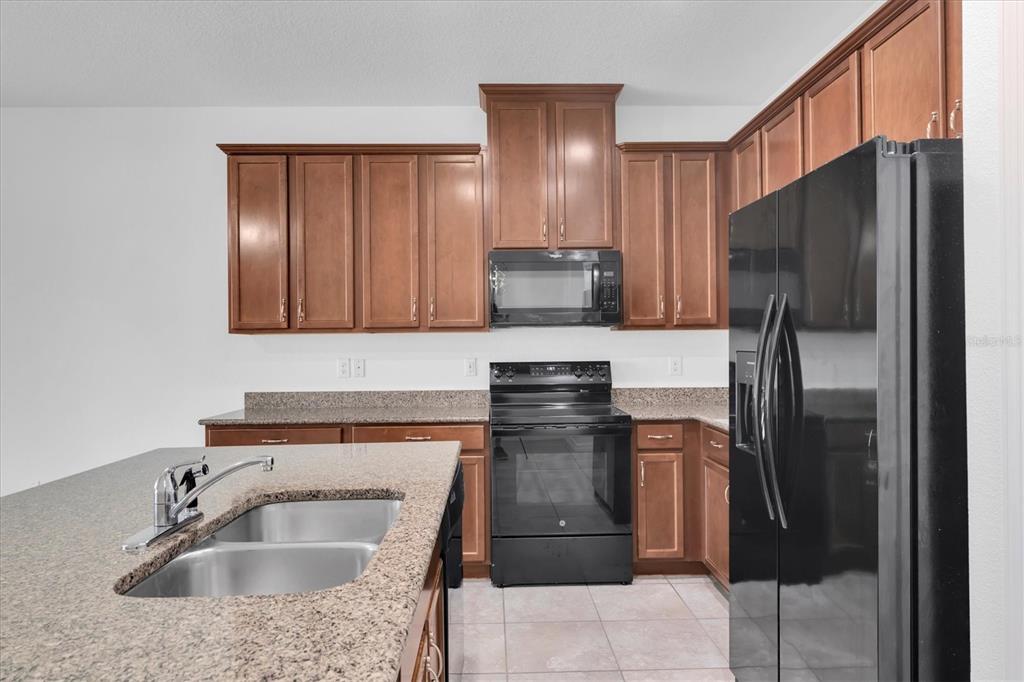 A kitchen features brown wooden cabinets, granite countertops, a black stove, and a black refrigerator — 4057 71ST TERRACE N, PINELLAS PARK, FL
