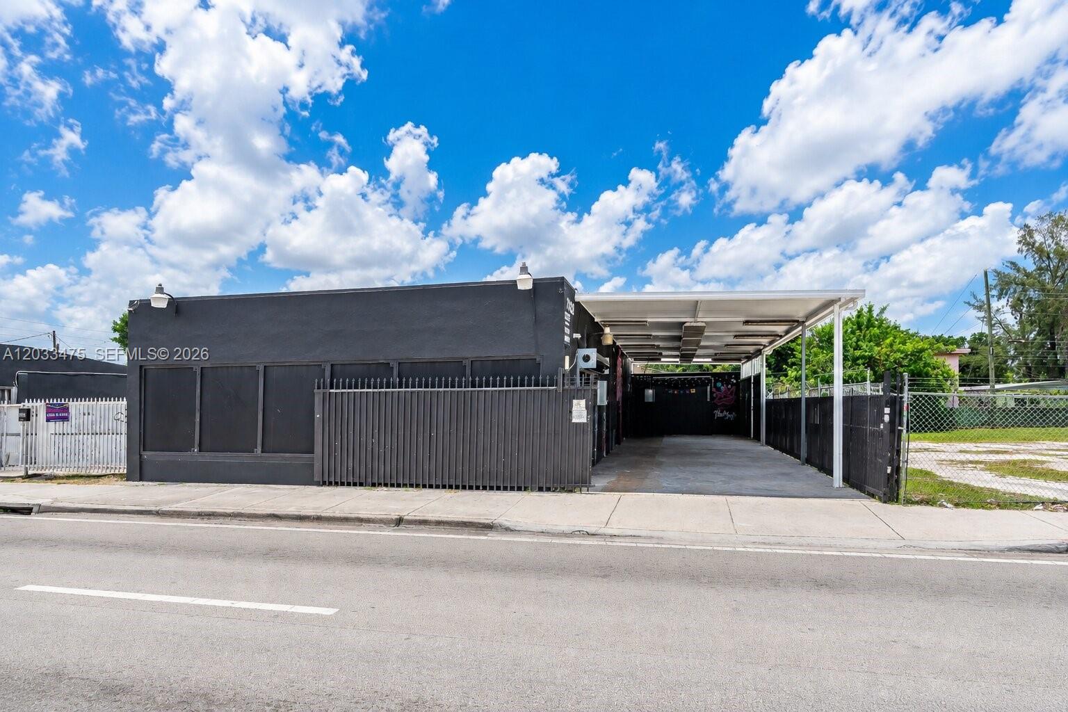 A black commercial building features a covered parking area and a fenced-in lot — 7025 NW 7th Ave, Miami FL 33150, MIAMI, FL
