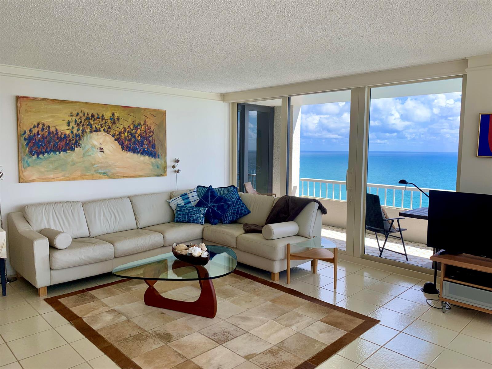 A living room with a white sectional sofa, glass coffee table, and ocean view balcony — 5540 N Ocean Drive # a, Riviera Beach FL 33404, RIVIERA BEACH, FL