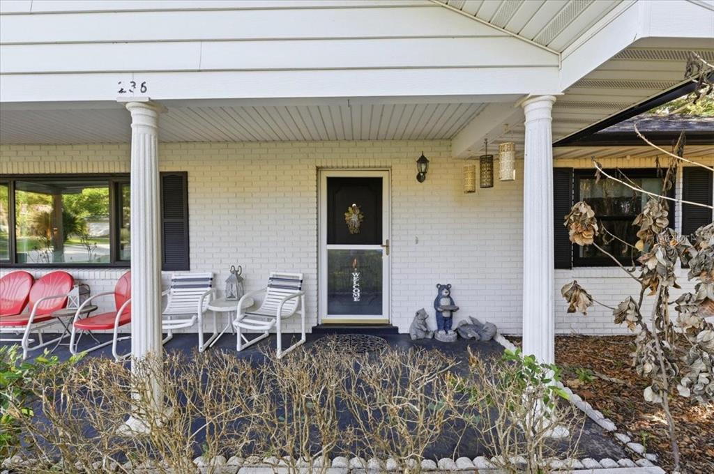 A covered front porch features white brick walls, two columns, and several chairs — 236 W LAKE INA DRIVE, WINTER HAVEN, FL