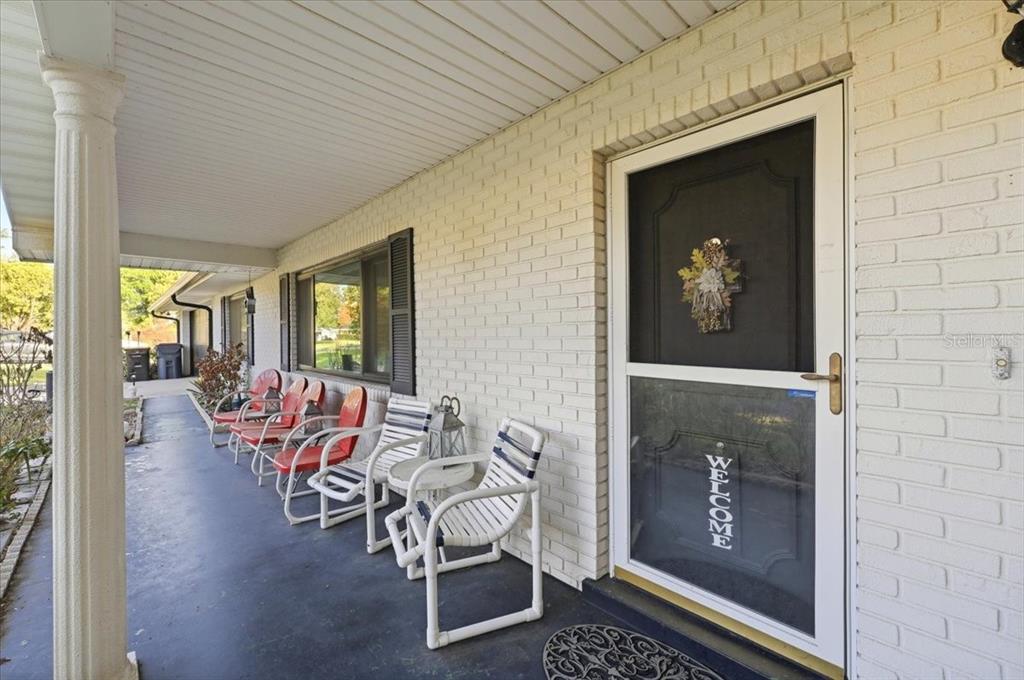 A covered porch features white brick walls, a storm door, and a row of chairs — 236 W LAKE INA DRIVE, WINTER HAVEN, FL