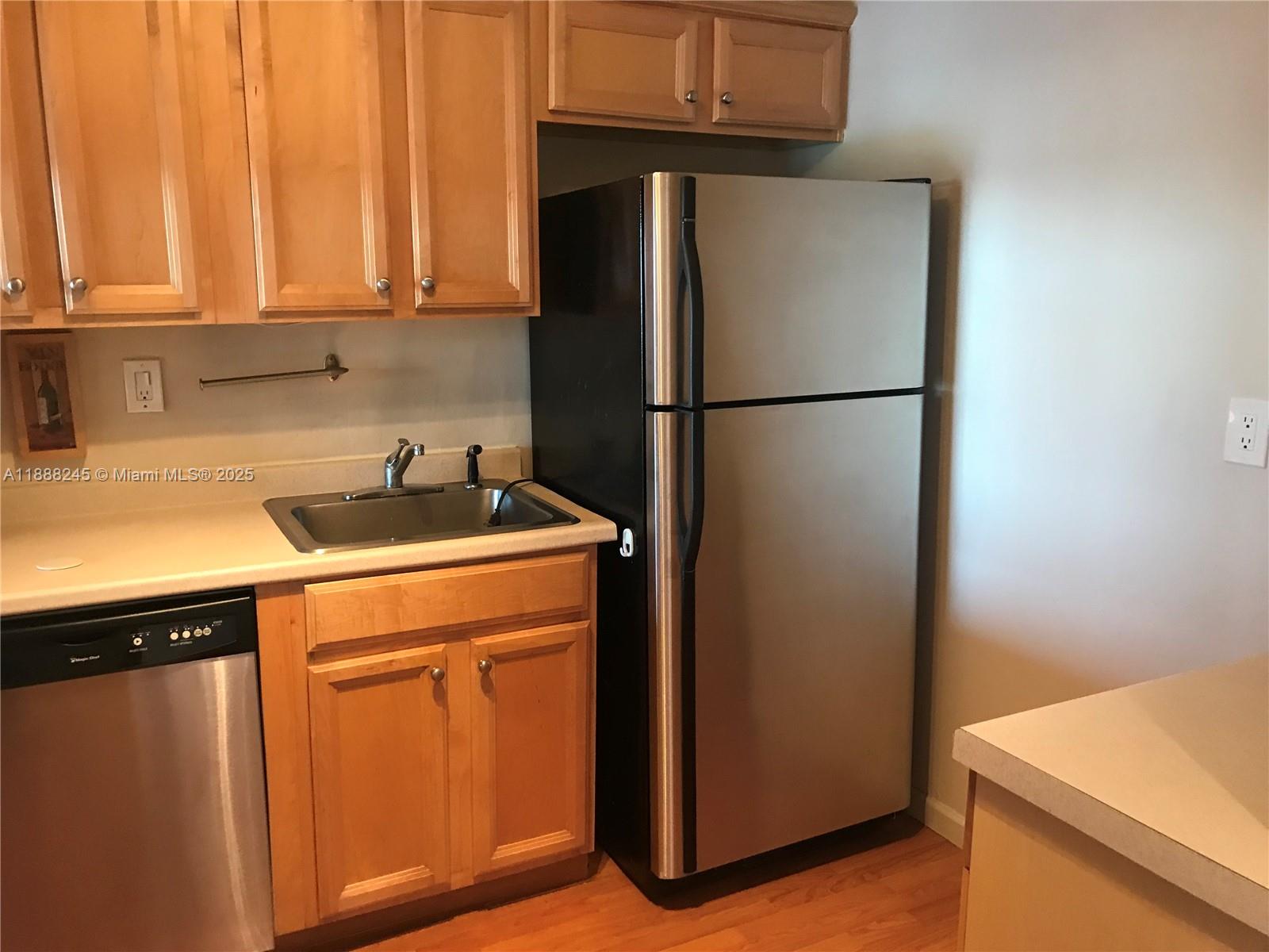 A kitchen features light wood cabinets, a stainless steel refrigerator, and a small sink — 1000 Parkview Dr # 627, Hallandale Beach FL 33009, HALLANDALE BEACH, FL