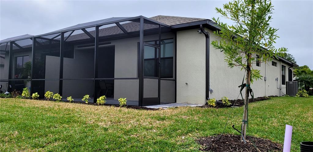 A tan house features a black-framed screened-in patio and a young tree in the yard — 2168 GARDENIA AVENUE, PORT CHARLOTTE, FL