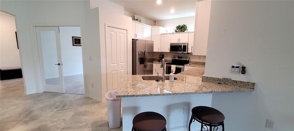 A kitchen features white cabinets, granite countertops, a stainless steel refrigerator, and a breakfast bar — 2168 GARDENIA AVENUE, PORT CHARLOTTE, FL
