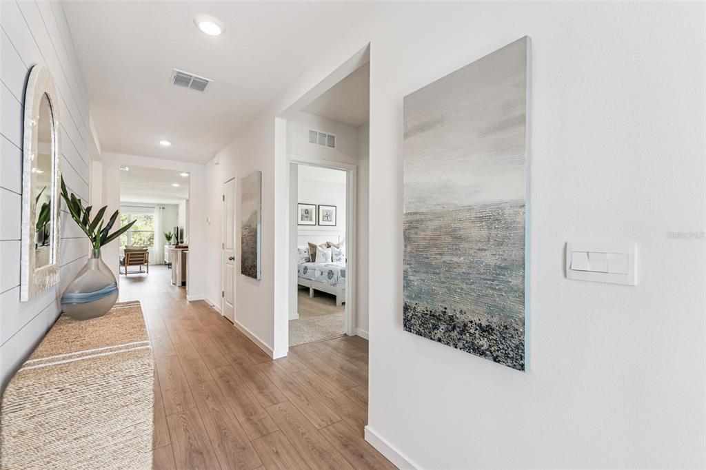 A hallway with wood-look flooring, white walls, two abstract paintings, and a console table — 5151 NICKERBEAN STREET, APOPKA, FL