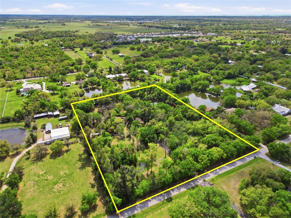 An aerial view shows a wooded residential lot outlined in yellow near a pond — 7336 CURLEW STREET, SARASOTA, FL