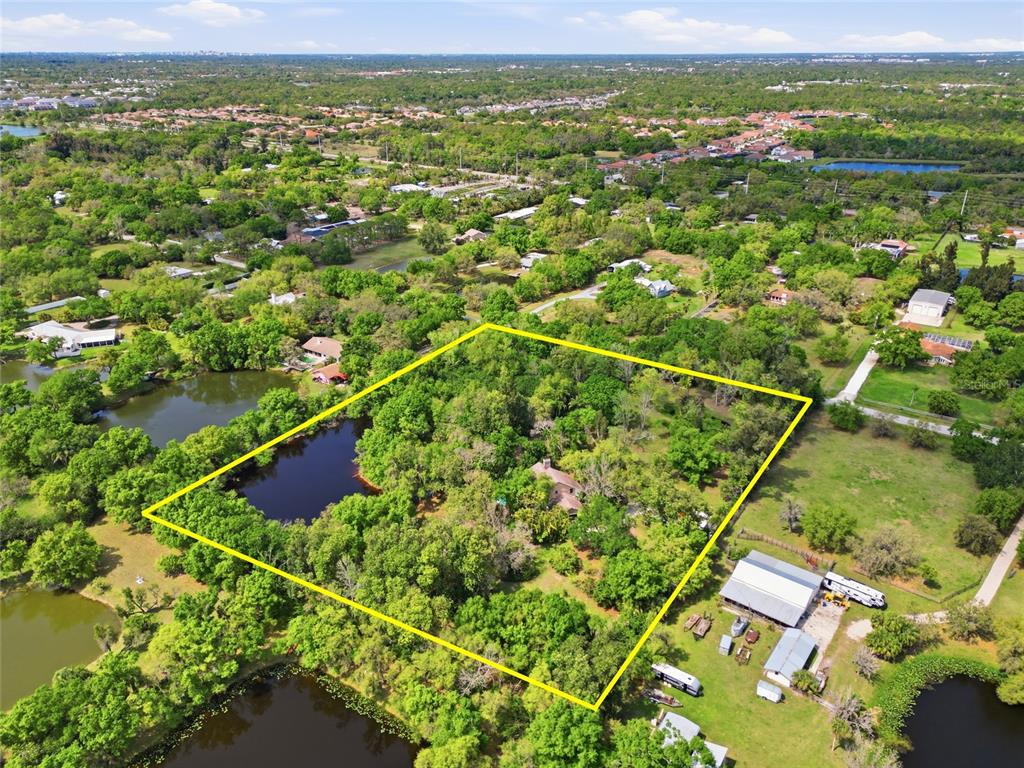 An aerial view shows a wooded residential lot outlined in yellow, featuring a pond and house — 7336 CURLEW STREET, SARASOTA, FL