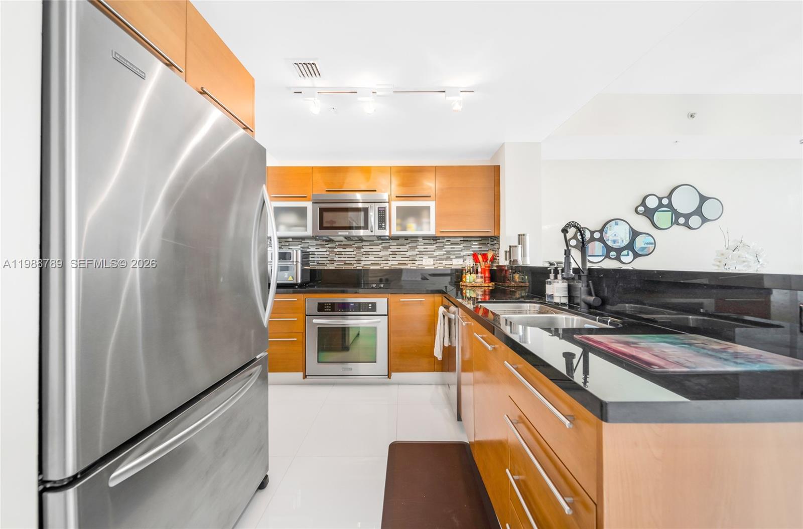 A modern kitchen features stainless steel appliances, wood cabinetry, and black granite countertops — 253 NE 2nd St # 1109, Miami FL 33132, MIAMI, FL