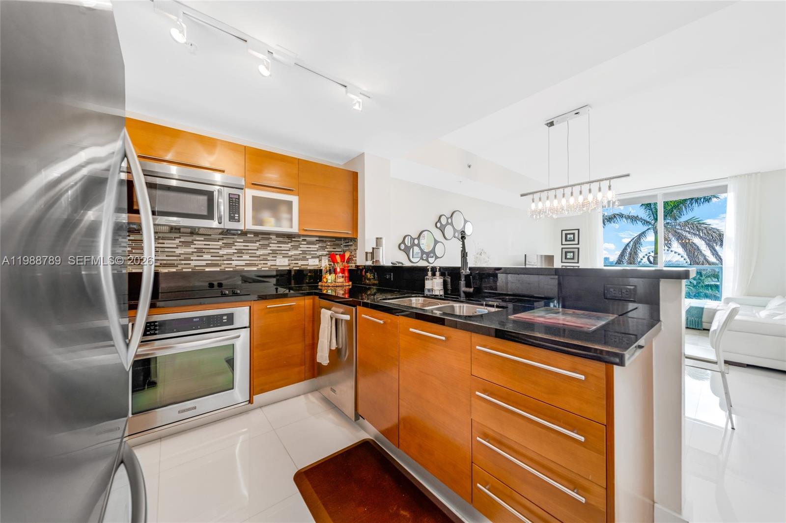 A modern kitchen features wood cabinets, black countertops, stainless steel appliances, and tile flooring — 253 NE 2nd St # 1109, Miami FL 33132, MIAMI, FL