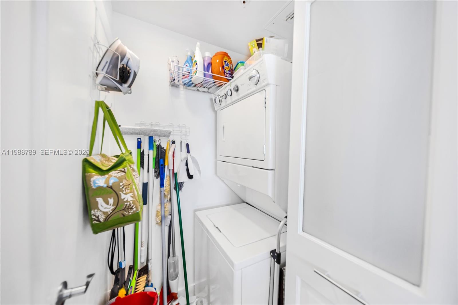 A laundry closet contains a stacked washer and dryer, cleaning supplies, and hanging tools — 253 NE 2nd St # 1109, Miami FL 33132, MIAMI, FL