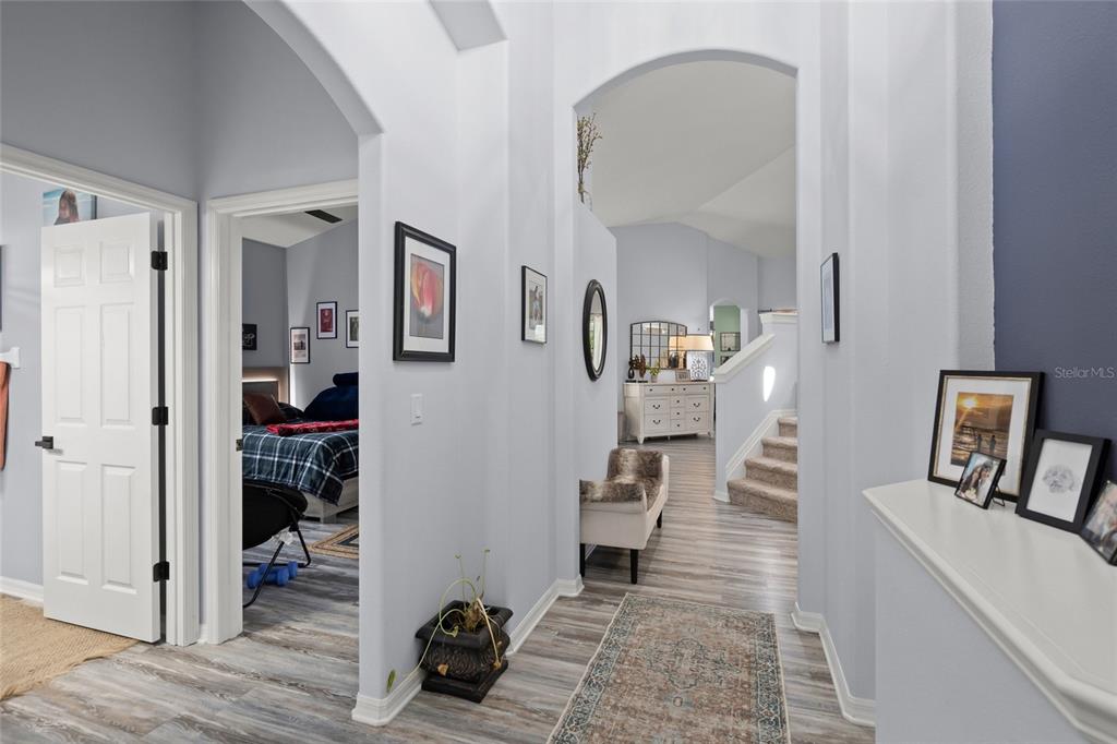 A hallway with light gray walls and wood-look flooring leads to a staircase and bedroom — 6723 TAILFEATHER WAY, BRADENTON, FL