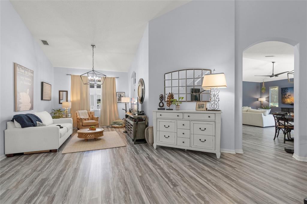A living room with light gray walls, wood-look flooring, a white sofa, and a white dresser — 6723 TAILFEATHER WAY, BRADENTON, FL