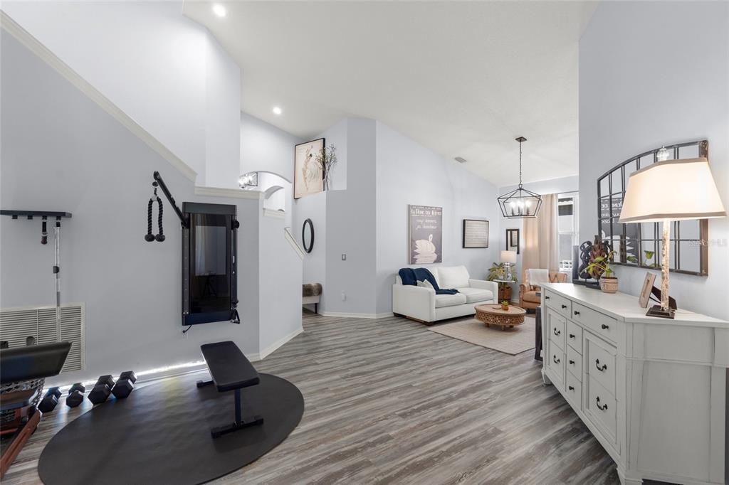 A living room features light blue walls, wood-look flooring, a home gym area, and white furniture — 6723 TAILFEATHER WAY, BRADENTON, FL