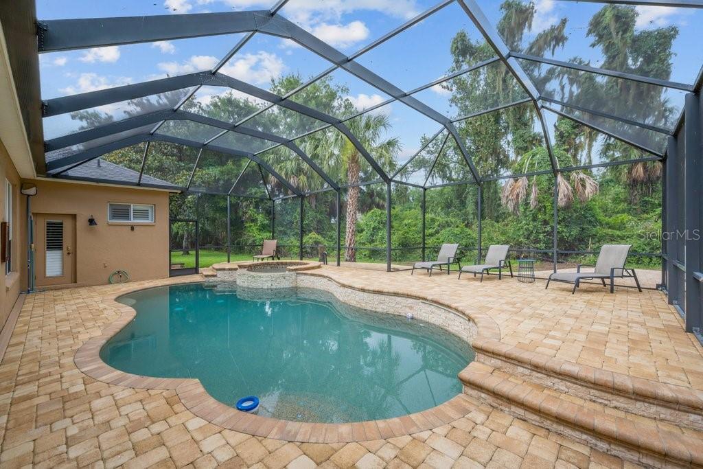 A screened-in patio features a swimming pool, a raised spa, and beige paver decking — 6122 KESTRELPARK DRIVE, LITHIA, FL