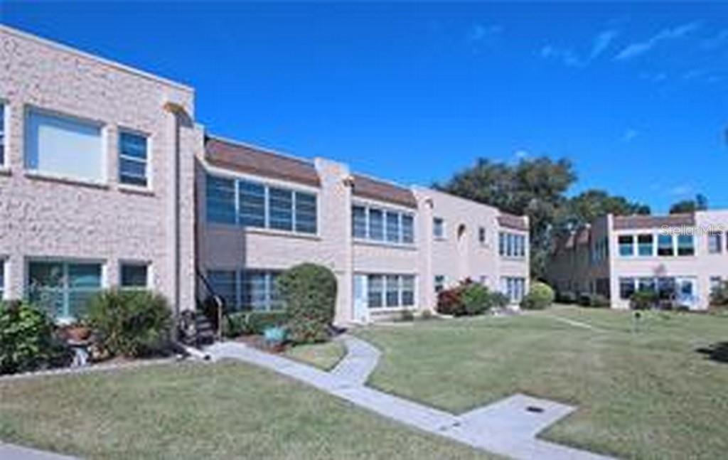 A multi-story tan brick apartment building with a sidewalk and lawn in the foreground — 221 CEDARWOOD CIRCLE UNIT 221, SEMINOLE, FL