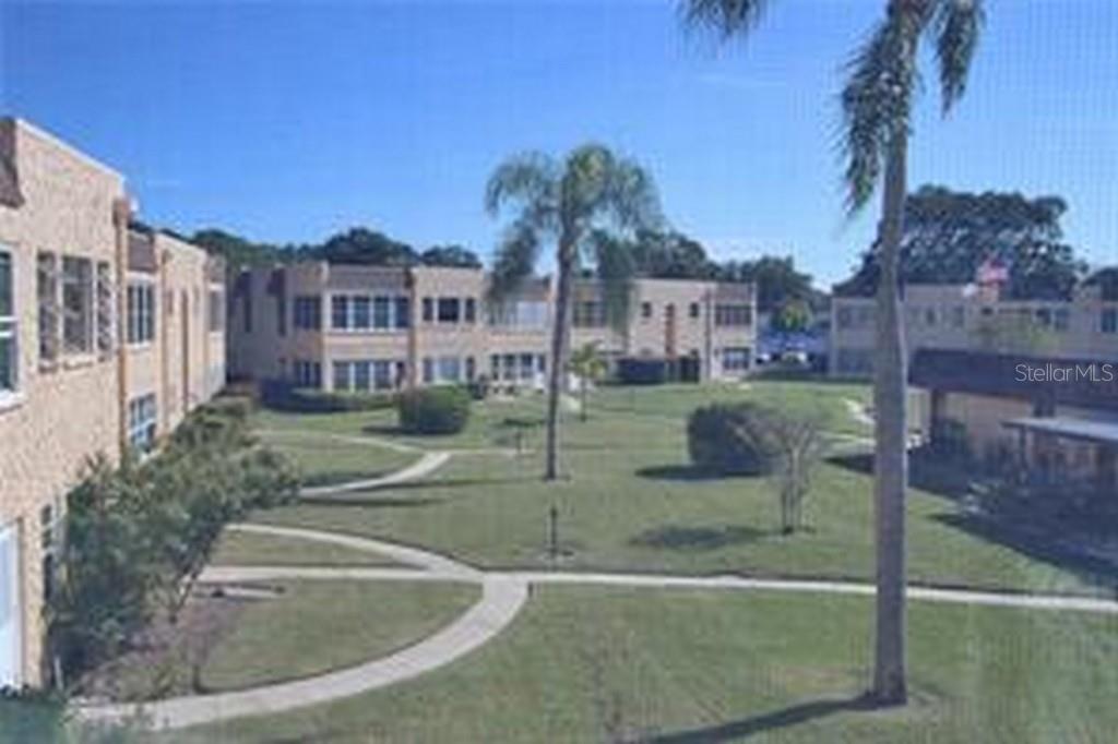 An exterior view of a multi-story apartment complex with a central grassy courtyard and palm trees — 221 CEDARWOOD CIRCLE UNIT 221, SEMINOLE, FL