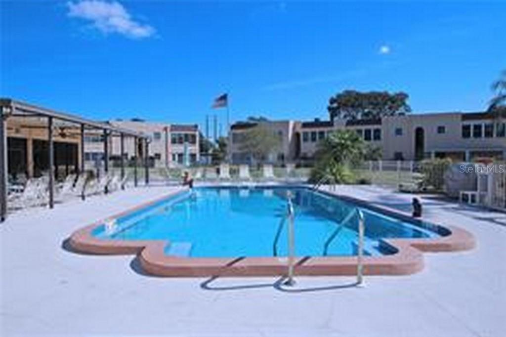 An outdoor swimming pool is surrounded by a concrete deck and multi-story apartment buildings — 221 CEDARWOOD CIRCLE UNIT 221, SEMINOLE, FL