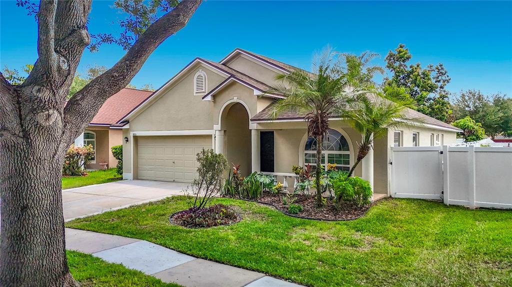 A tan single-story house with a two-car garage, a palm tree, and a white fence — 805 LESA GLEN PLACE, BRANDON, FL