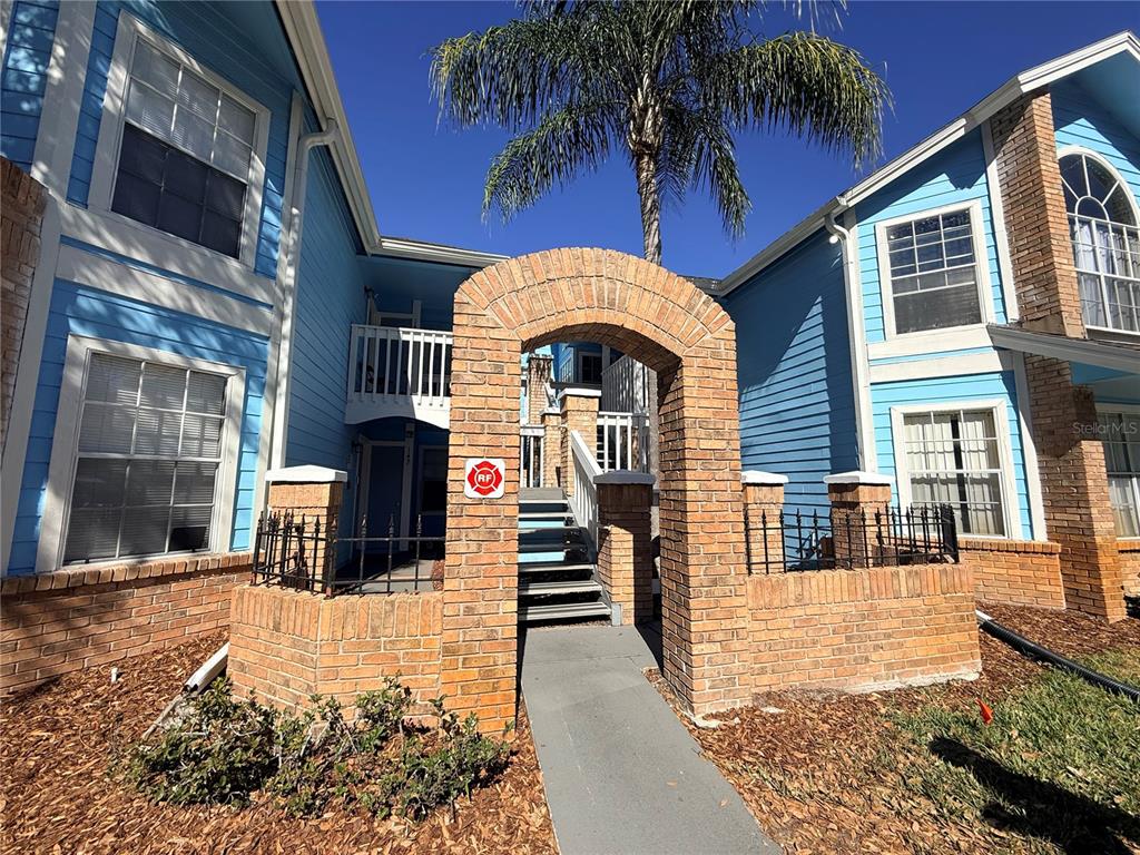 A brick archway leads to a staircase between two blue-sided apartment buildings — 2725 N POINCIANA BOULEVARD UNIT 147, KISSIMMEE, FL