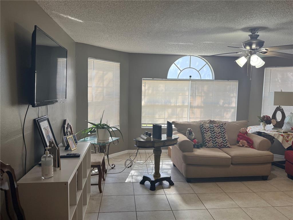 A living room features tile flooring, a ceiling fan, a wall-mounted television, and large windows — 2725 N POINCIANA BOULEVARD UNIT 147, KISSIMMEE, FL