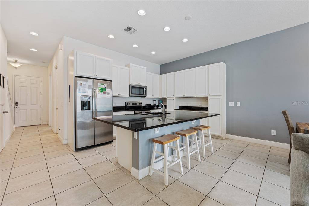 A kitchen features white cabinets, black countertops, a center island with stools, and tile flooring — 318 CAPTIVA DRIVE, DAVENPORT, FL