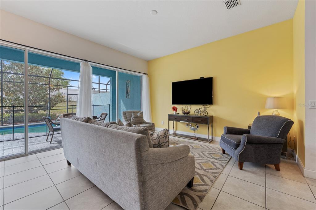 A living room features a yellow wall, a gray sofa, a television, and a pool view — 318 CAPTIVA DRIVE, DAVENPORT, FL