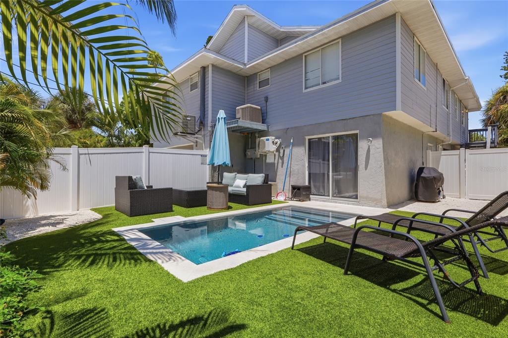 A backyard features a small rectangular swimming pool, artificial turf, patio furniture, and a two-story house — 207 71ST STREET UNIT E, HOLMES BEACH, FL