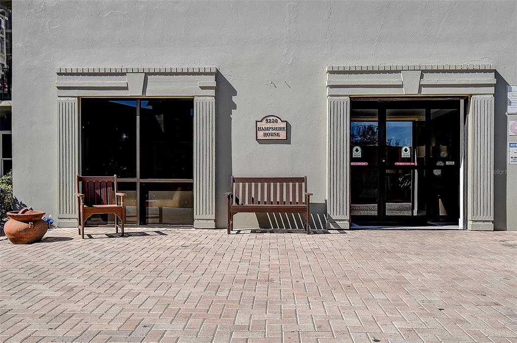 A brick-paved entrance area features a wooden bench, a chair, and a building sign — 5220 BRITTANY DRIVE S UNIT 509, ST PETERSBURG, FL