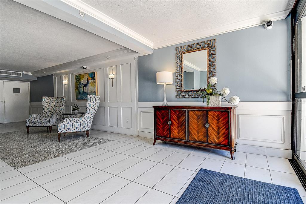 A lobby features white tile floors, a wooden console table, a mirror, and two patterned chairs — 5220 BRITTANY DRIVE S UNIT 509, ST PETERSBURG, FL