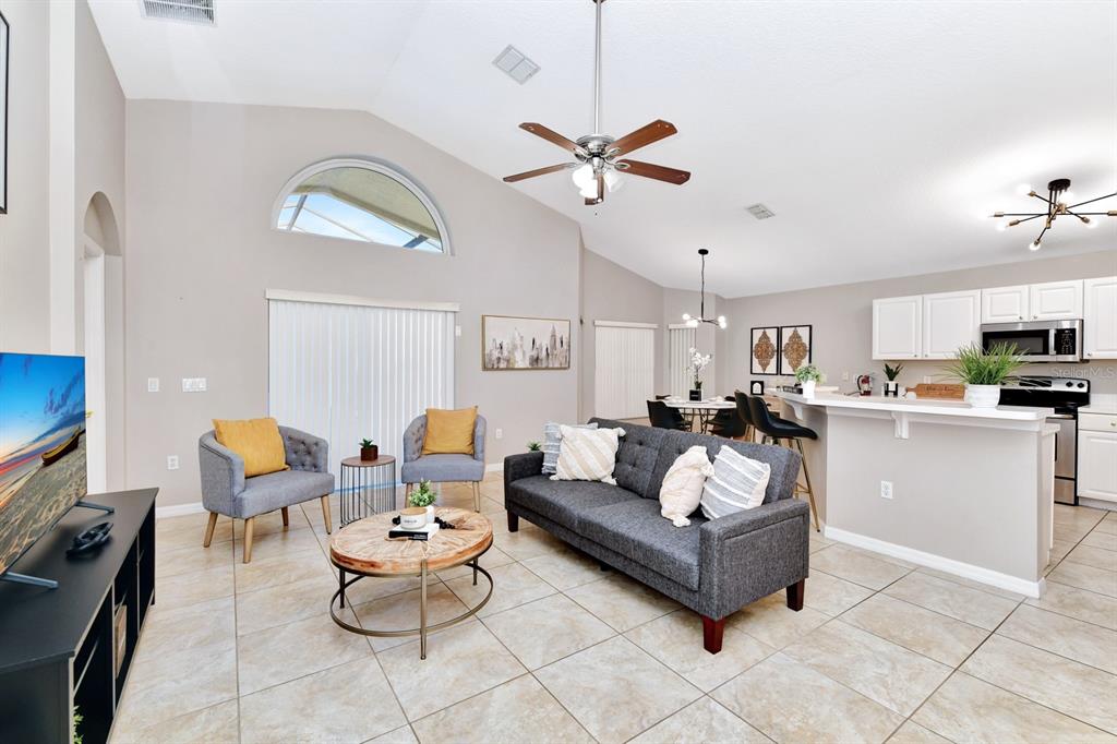 A living room with tile floors, a grey sofa, two armchairs, and an open kitchen — 4661 CUMBRIAN LAKES DRIVE, KISSIMMEE, FL