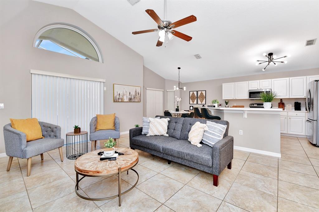 A living room with tile floors, a grey sofa, and an open kitchen with white cabinets — 4661 CUMBRIAN LAKES DRIVE, KISSIMMEE, FL