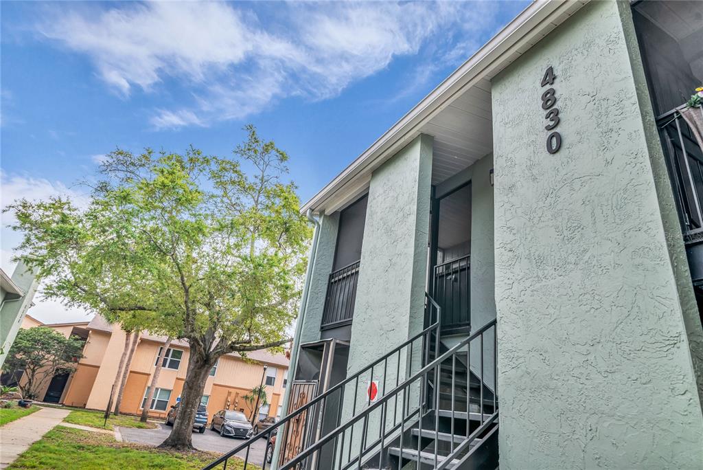 An exterior view of a light green apartment building with an outdoor staircase — 4830 S SEMORAN BOULEVARD UNIT 1108, ORLANDO, FL