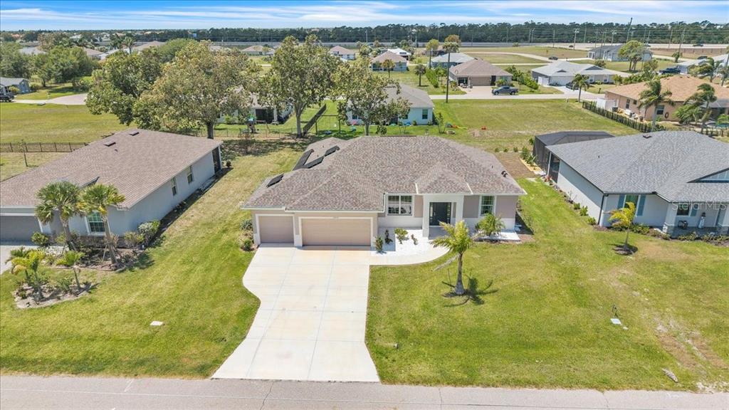 An aerial view shows a single-story suburban house with a tan exterior and concrete driveway — 16047 DINAL DRIVE, PUNTA GORDA, FL