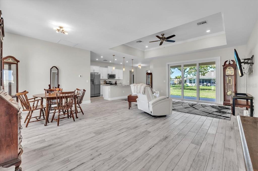 An open-concept living and dining area features light wood-look tile flooring and a tray ceiling — 16047 DINAL DRIVE, PUNTA GORDA, FL