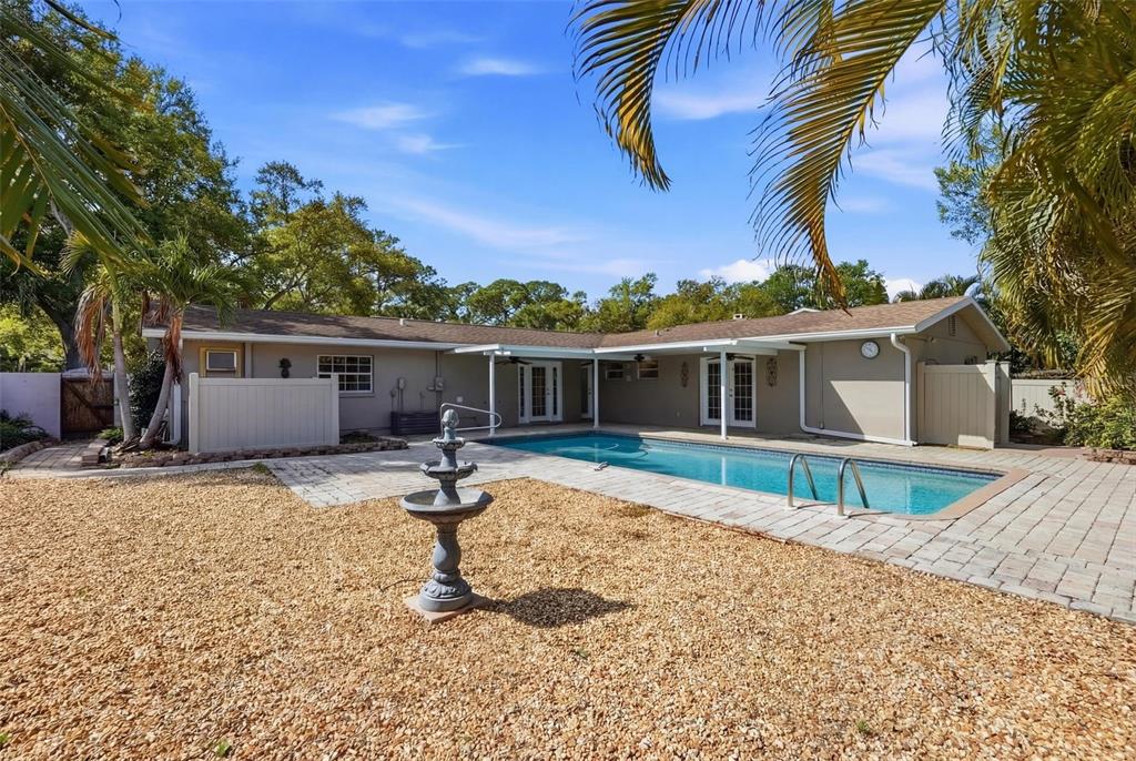 A backyard features a swimming pool, a stone patio, a fountain, and a tan house — 8235 39TH AVENUE N, ST PETERSBURG, FL