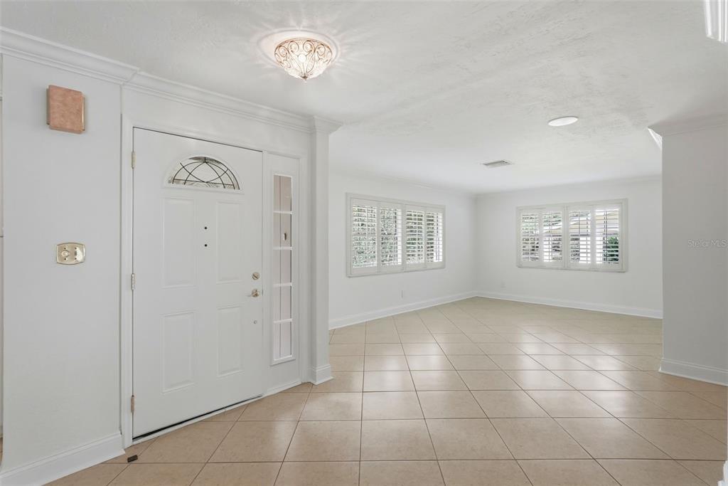 A bright entryway with tile flooring leads into a spacious living area with white walls — 8235 39TH AVENUE N, ST PETERSBURG, FL