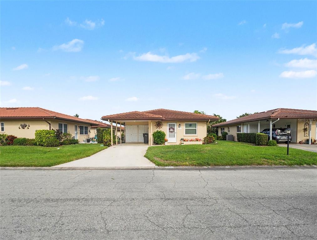 A single-story house with a carport and a tiled roof sits behind a paved street — 6608 AUBURN AVENUE, BRADENTON, FL